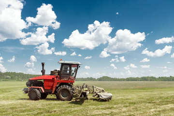 Agricultural machinery, harvester mowing grass in a field against a blue sky. Hay harvesting, grass...
