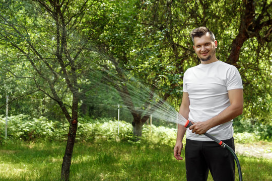 A man is watering from a hose, the concept of gardening. Hand held garden hose with water spray, watering flowers, splashing water. Copy space