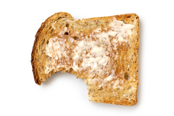 Buttered slice of whole wheat toast isolated on white from above. Bite missing.
