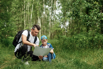 Naklejka na ściany i meble A man with a backpack, a father and his son on a hike look at the map, walking during walks in the woods. Family life, pastime with the family, the upbringing of children.
