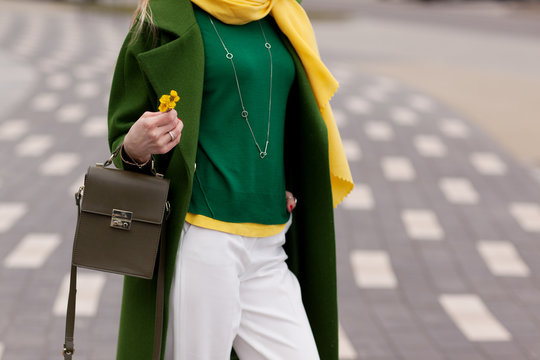 Street, bright style. A young girl in white trousers, warm greens polto. Yellow scarf. Green jacket. A brown handbag. Details. Flowers