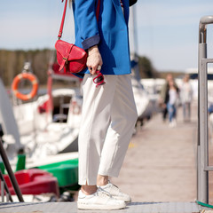 Street, bright style. Young woman in a blue jacket, white sneakers, white trousers, a red handbag, Sunglassesand and a red case for sunglasses. Details. Sguare image photo