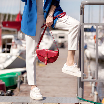 Street, bright style. Young woman in a blue jacket, white sneakers, white trousers, a red handbag, Sunglassesand and a red case for sunglasses. Details. Sguare image photo