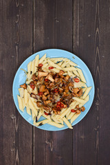 Healthy nutritious meal with forest mushrooms. Pasta penne with golden chanterelle mushrooms and chili peppers in blue plate on dark wooden background copyspace
