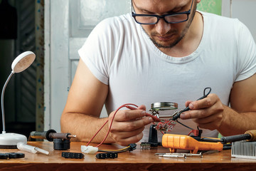 The man remotes the microcircuit. Workplace with soldering iron, microcircuit, magnifying glass,...