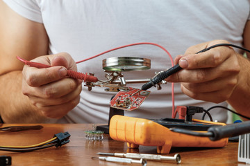The man remotes the microcircuit. Workplace with soldering iron, microcircuit, magnifying glass,...