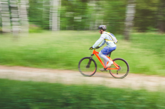 A cyclist in a helmet rides through the forest on a bicycle path, motion blur