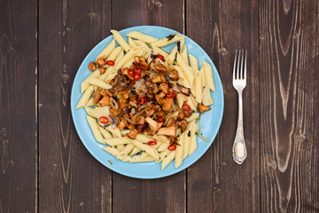 Vegetarian healthy food. Forest mushrooms golden chanterelles and pasta penne with chili pepper in blue plate on dark rustic background copyspace