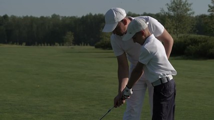 Happy man with his son golfers walking on perfect golf course at summer day