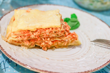 Lasagna bolognese slice on a white patterned plate with basil and fork on table