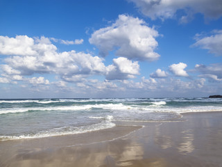 Waves spreading on a sandy Black Sea beach, cloud reflections on the sand, cumulus clouds in the sky