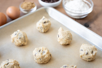 Chocolate chip cookie dough balls on parchment paper with ingredient dishes in the background