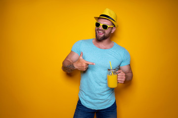 Creative male in sunglasses and summer clothes in yellow and blue colors standing relaxed, pointing...