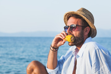 Young man eating corn on the beach © marjan4782