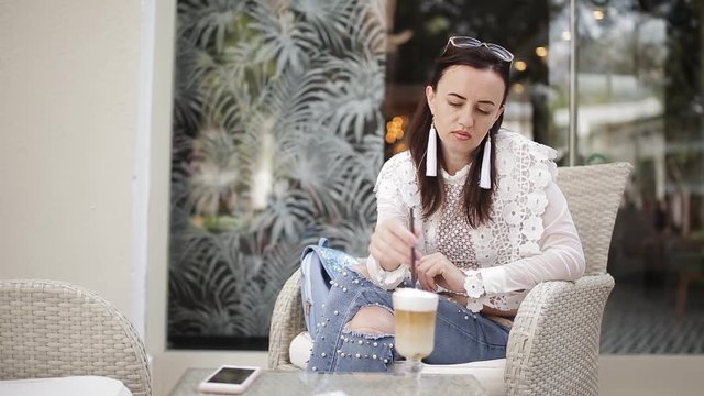 Girl in the cafe in the fresh air sitting in a chair drinking latte from a glass Cup through a straw