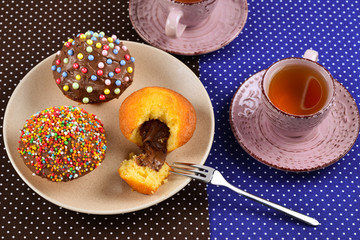 Baking with tea and chocolate on the table.  Two cups of tea with cupcakes and chocolate with a multicolored powder on the table.