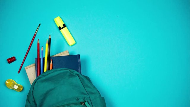 Colorful school supplies moving from school bag on blue background. Back to school concept. Stop motion
