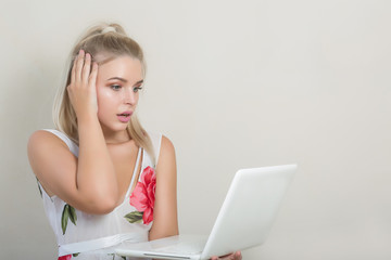 Shocked attractive blonde model looking into laptop, posing on the grey background, empty space