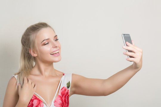 Charming cute girl making self portrait on smartphone against a grey background
