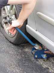 A man using a car jack to lift a car to fix a flat tire
