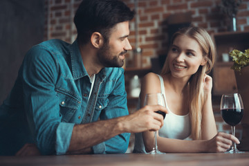 Beautiful young couple is drinking wine and smiling while cooking in kitchen at home.