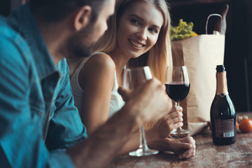 Beautiful young couple is drinking wine and smiling while cooking in kitchen at home.