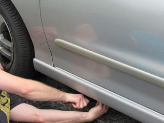 A man using a car jack to lift a car to fix a flat tire