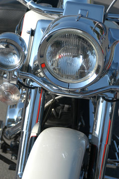 Vintage classic American motorcycle detail of headlight and front forks. Vintage cruiser motorbike parked outside in the sun, no people. American motorcycle on the road. White paint with black trim.