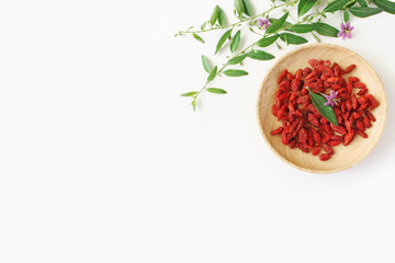 Heap of dried Goji berries fruit, Lycium barbarum in wooden bowl on white table. Blossoming...