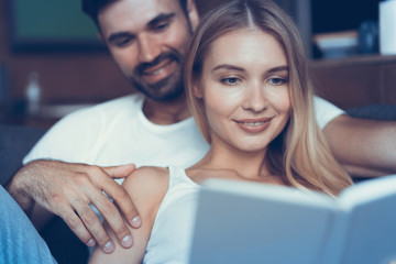 Spending nice time at home. Beautiful young loving couple bonding to each other and smiling while woman holding a book.