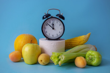 Alarm clock, fruits and toilet paper on a blue background. Natural remedy for constipation. The...