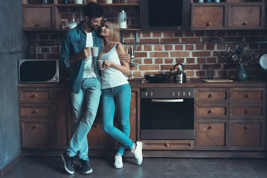 Young Happy Couple Hugging And Looking At Each Other In The Interior Of A New Kitchen, Happiness In A New Home.