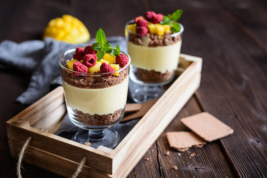 Layered mango dessert with cream cheese, crushed biscuits and freeze dried raspberries