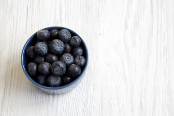 Blueberries in a blue bowl, top view. Fresh bilberry on white wooden table. Copy space.
