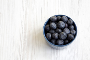 Blueberries in a blue bowl, top view. Fresh bilberry on white wooden surface. Copy space.