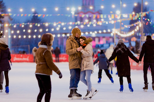 Ice skating rink and lovers together. A pair of young people in an embrace on a city skating rink lit by light bulbs and bright lights. Winter date for Christmas on the ice arena
