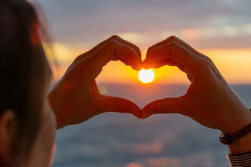 hands forming heart symbol during sunset 