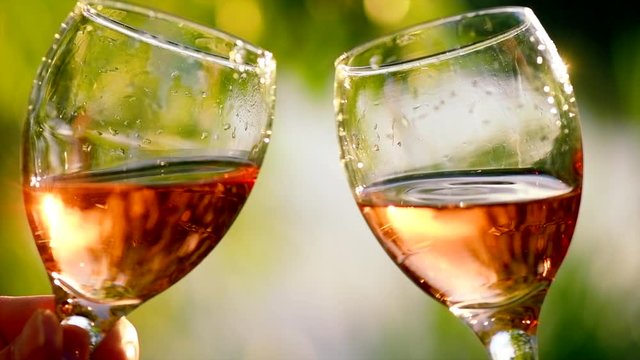 Friends raising wine glasses outdoors. Toasting and drinking rose wine. Group of people drinking wine. Two glasses over blurred green background. Slow motion 4K UHD video 3840x2160