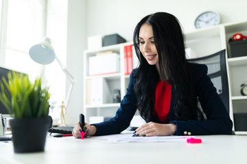 Beautiful young girl is working with documents in the office at the table. The girl highlights...