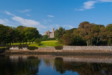 Fototapeta na wymiar Landmark and attraction. Lews Castle in Stornoway, United Kingdom seen from sea harbor. Castle with green grounds on blue sky. Victorian style architecture and design. Summer vacation and wanderlust