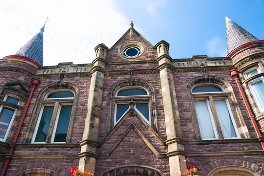 Town hall building in Stornoway, United Kingdom. Brick house with towers on sunny blue sky. Architecture and structure. Style and design. Vacation and wanderlust