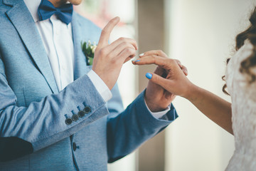 A stylish bridegroom wearing a ring on the finger of his elegant bride bow-tie