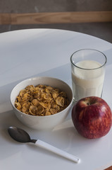 Breakfast with a glass of milk, a bowl with cereals and an apple.