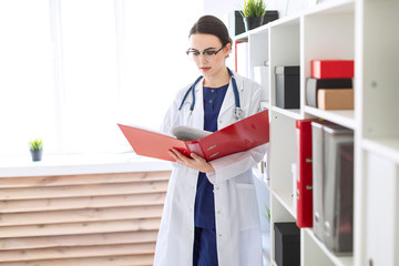 A beautiful young girl in a white robe is standing near the shelter and flips through a red folder...