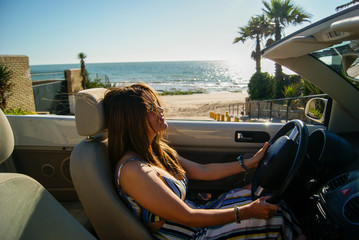 Beautiful girl sitting in a convertible car on the beach - obrazy, fototapety, plakaty