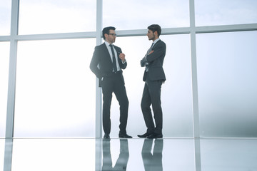 two businessmen standing near a large office window