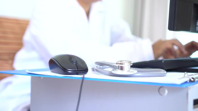 Healthcare and medical concept, Doctor working searching information Patient database through internet computer, have Stethoscope with prescription clipboard record on hospital office, selective focus