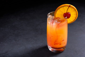 Tequila sunrise cocktail on dark stone background with copy space.