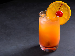 Tequila sunrise cocktail on dark stone background with copy space.