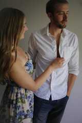 Romantic Couple Side view portrait of a Young Caucasian Couple Woman in Floral Dress Unbuttoning Man's White Collared Button Up Dress Shirt Natural Lighting on a White Studio Backdrop